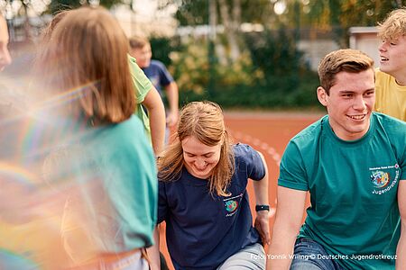 Betreuer und Kinder des Jugendrotkreuz sitzen im Freien auf einem Sprtplatz