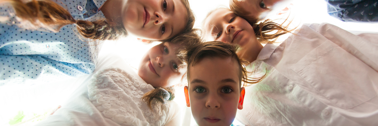 Tagesgruppen Kinder stehen im Kreis und schauen nach unten in die Kamera