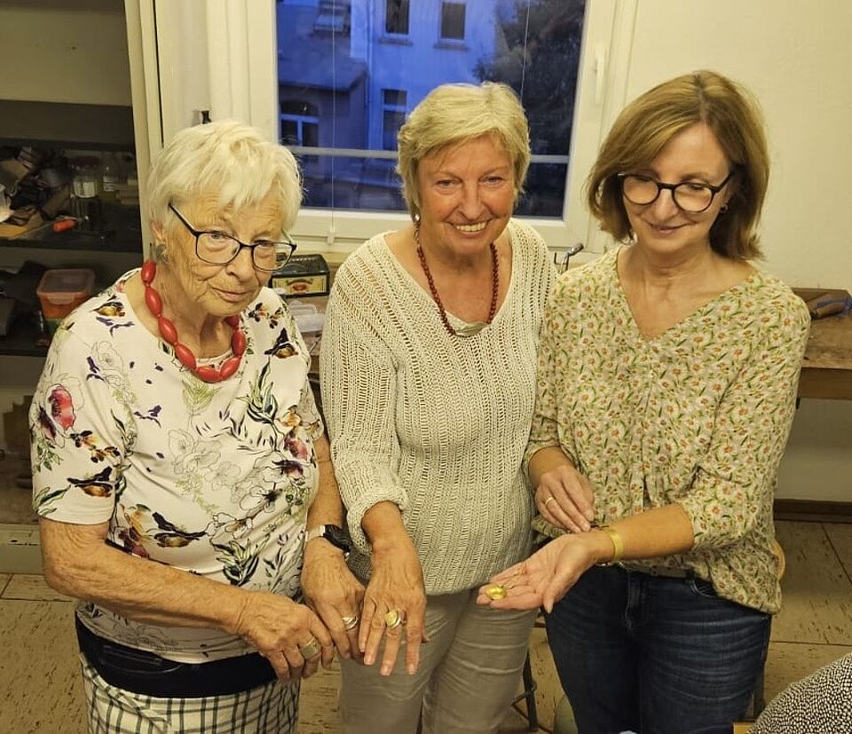 Kursleitung und zwei Teilnehmerinnen zeigen Ihren selbst erstellten Schmuck