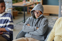 Jungendlicher sitzt mit verschränkten Armen auf einem Stuhl