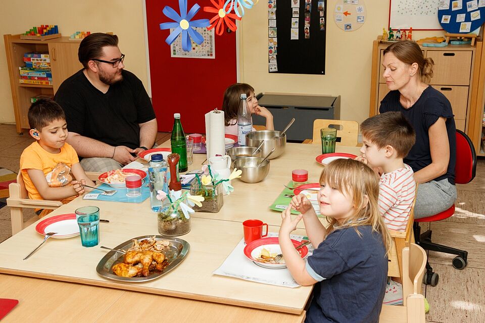 Kinder und Mitarbeitende sitzen gemeinsam am Tisch und essen
