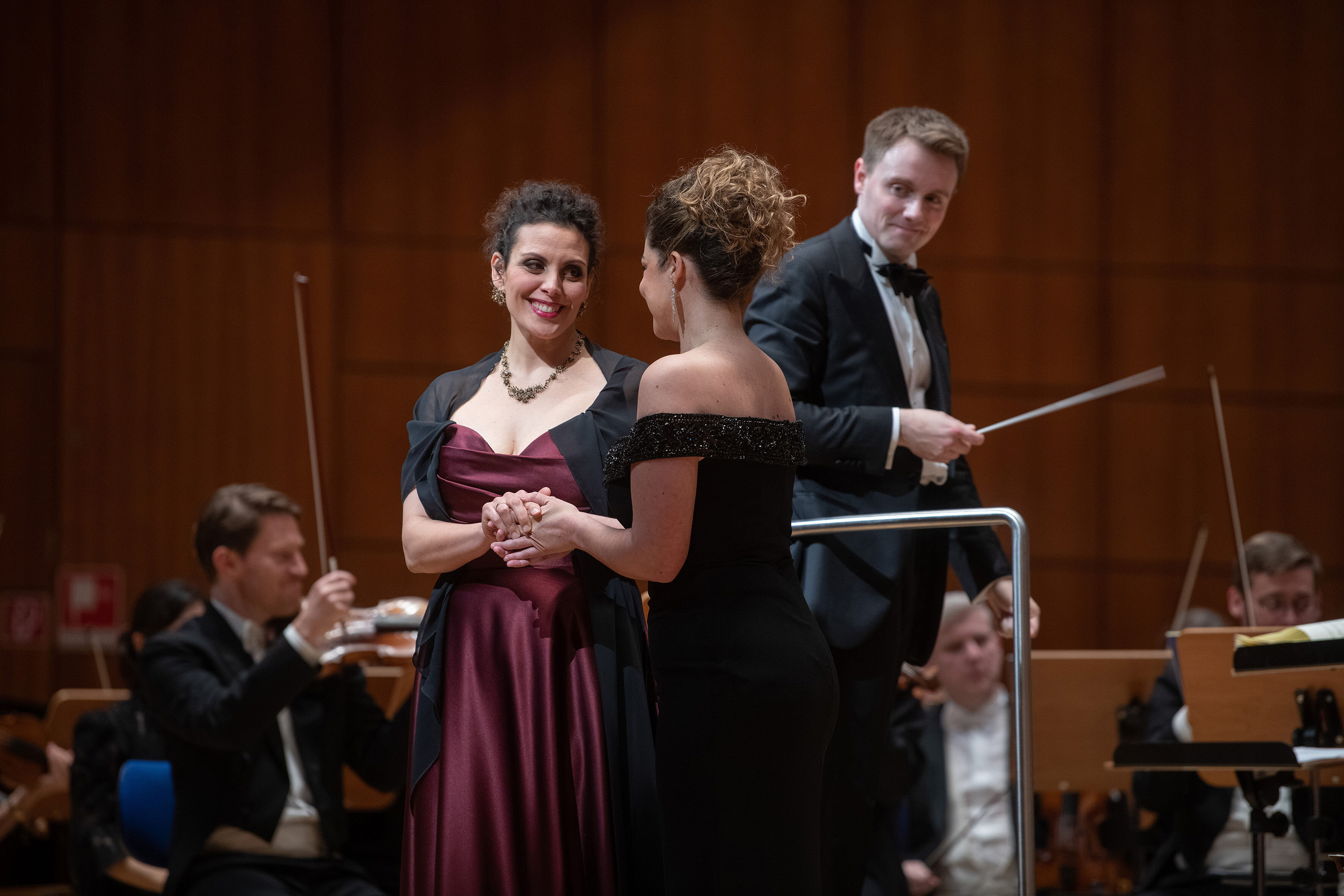 Sägerinnen, im Hintergrund Musiker*innen und Dirigent